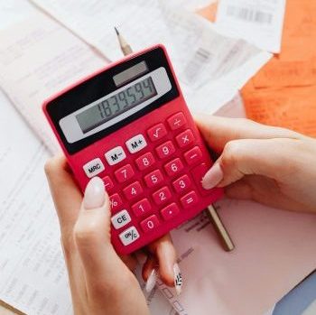 A person calculating finances on a red calculator surrounded by documents.